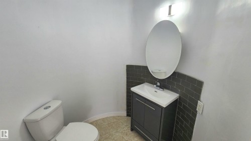 Bathroom featuring a white toilet, dark gray vanity with integrated sink, chrome faucet, and an oval mirror - 9535 147 Avenue, Edmonton, AB - Indoor Photo Showing Bathroom