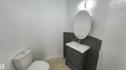 Bathroom featuring a white toilet, dark gray vanity with integrated sink, chrome faucet, and an oval mirror - 
