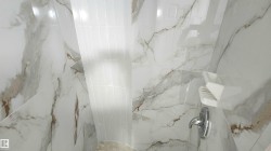 Shower stall featuring large format white tiled walls with brown veining and a contrasting vertical band of white subway tile - 
