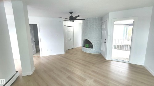Spacious room featuring light wood-finish flooring, a white-painted brick fireplace, a matte black ceiling fan, and a glass-paneled exterior door - 9535 147 Avenue, Edmonton, AB - Indoor Photo Showing Other Room