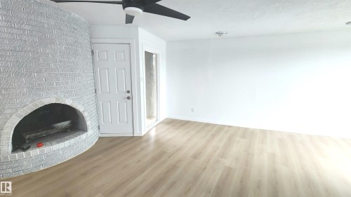 Curved brick fireplace with a hearth, wood-finish flooring, white walls, and a ceiling fan with integrated lighting - 9535 147 Avenue, Edmonton, AB - Indoor With Fireplace