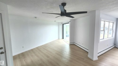 Spacious interior featuring light wood-finish flooring, a modern black ceiling fan, white baseboard trim, and a sliding glass door - 9535 147 Avenue, Edmonton, AB - Indoor Photo Showing Other Room