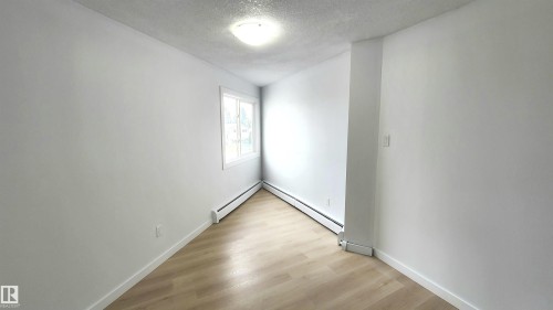 Bright room featuring a window with white trim, wood-finish flooring, and white baseboard heaters - 9535 147 Avenue, Edmonton, AB - Indoor Photo Showing Other Room