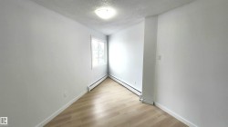 Bright room featuring a window with white trim, wood-finish flooring, and white baseboard heaters - 