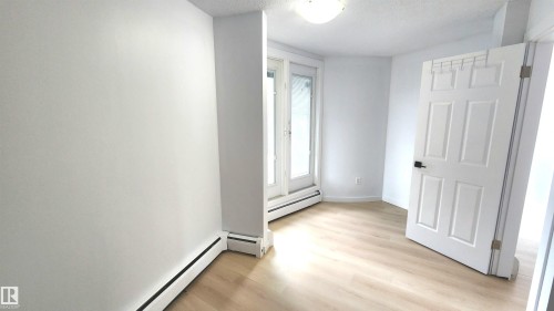 Bright interior space featuring light wood-finish flooring, white walls, and a white six-panel door with matte black hardware - 9535 147 Avenue, Edmonton, AB - Indoor Photo Showing Other Room