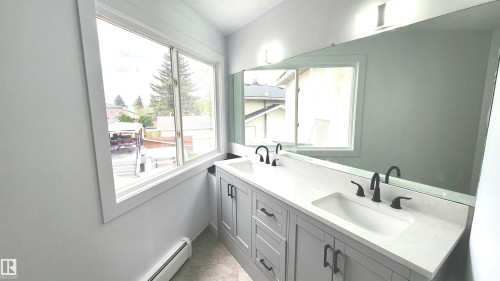 Dual vanity with white undermount sinks, stone countertops, and matte black hardware - 9535 147 Avenue, Edmonton, AB - Indoor Photo Showing Bathroom