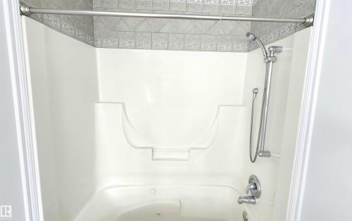 Combination shower and jetted tub unit featuring a built-in seat, a handheld shower fixture, and chrome hardware - 9535 147 Avenue, Edmonton, AB - Indoor Photo Showing Bathroom