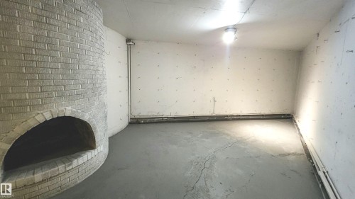 Curved brick fireplace feature, concrete flooring, and exposed utility piping - 9535 147 Avenue, Edmonton, AB - Indoor Photo Showing Other Room