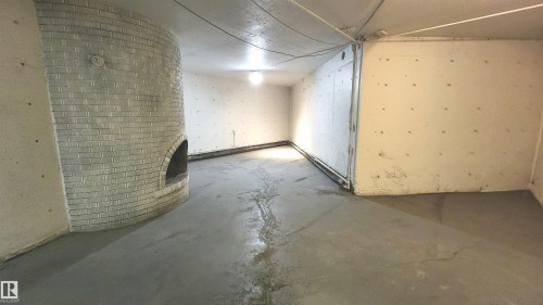 Utility room featuring a curved brick fireplace structure with an arched opening, concrete flooring, and exposed ceiling utilities - 9535 147 Avenue, Edmonton, AB - Indoor Photo Showing Garage