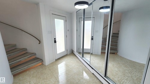 Entryway featuring light-toned tile flooring, a curved staircase with wood-finish treads and a metal handrail, and a frosted glass door - 9535 147 Avenue, Edmonton, AB - Indoor Photo Showing Other Room