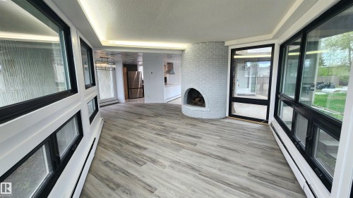 Sunroom featuring wood-finish flooring, a white brick fireplace, black-framed windows, and built-in baseboard heating - 9535 147 Avenue, Edmonton, AB - Indoor Photo Showing Other Room