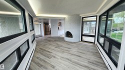 Sunroom featuring wood-finish flooring, a white brick fireplace, black-framed windows, and built-in baseboard heating - 