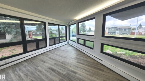 Sunroom featuring extensive fenestration with dark frames, light wood-finish flooring, and perimeter baseboard heating - 9535 147 Avenue, Edmonton, AB - Indoor Photo Showing Other Room