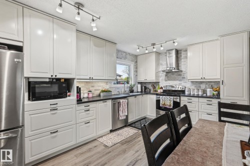 Well-appointed kitchen featuring abundant light-toned cabinetry, dark countertops, a mosaic tile backsplash, stainless steel appliances, and wood-finish flooring - 15232 120 Nw, Edmonton, AB 