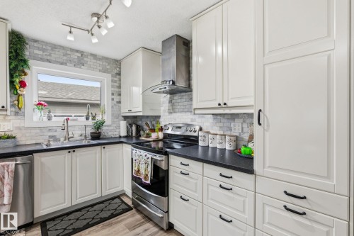 Kitchen featuring white shaker-style cabinetry, black countertops, stainless steel appliances, and a mosaic tile backsplash - 15232 120 Nw, Edmonton, AB 
