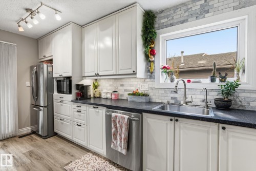 Kitchen featuring white cabinetry, dark countertops, a stainless steel sink with a gooseneck faucet, a light-toned wood-finish flooring, and a white subway tile backsplash - 15232 120 Nw, Edmonton, AB 