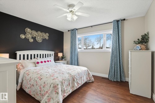 Bedroom featuring wood-finish flooring, a contemporary ceiling fan, and a large window with exterior visibility - 15232 120 Nw, Edmonton, AB 