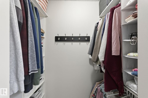 Walk-in closet featuring white wall-mounted shelving, multiple hanging rods, and a central wall-mounted coat rack with six hooks - 15232 120 Nw, Edmonton, AB 