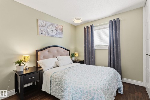 Bedroom featuring wood-finish flooring, a window with blinds and curtains, a light green wall color, and a white ceiling with a flush-mount light fixture - 15232 120 Nw, Edmonton, AB 