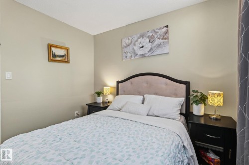 Bedroom featuring a tufted upholstered headboard, neutral wall color, and dark wood-finish bedside tables - 15232 120 Nw, Edmonton, AB 