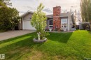 Front exterior featuring siding and brick accents, a mature front yard with a landscaped planter, an attached garage, and a detached shed - 15232 120 Nw, Edmonton, AB 