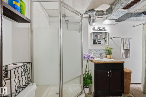 Bathroom featuring a glass-enclosed shower, a vanity with a wood-finish countertop, a single sink, and a tiled backsplash - 15232 120 Nw, Edmonton, AB 