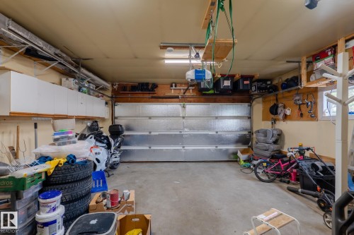 Spacious garage featuring a concrete floor, overhead storage shelving, and a paneled garage door - 15232 120 Nw, Edmonton, AB 