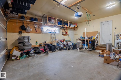 Spacious garage with concrete flooring, overhead fluorescent lighting, a window, and extensive built-in wooden shelving for organization - 15232 120 Nw, Edmonton, AB 