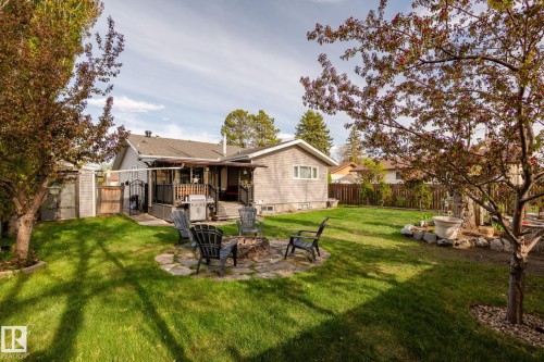 Spacious backyard featuring a stone fire pit area, expansive lawn, and mature trees - 15232 120 Nw, Edmonton, AB 