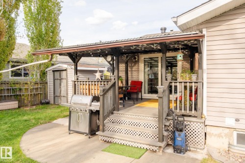 Covered outdoor deck with pergola, featuring a sliding glass door, white lattice skirting, and concrete patio - 15232 120 Nw, Edmonton, AB 