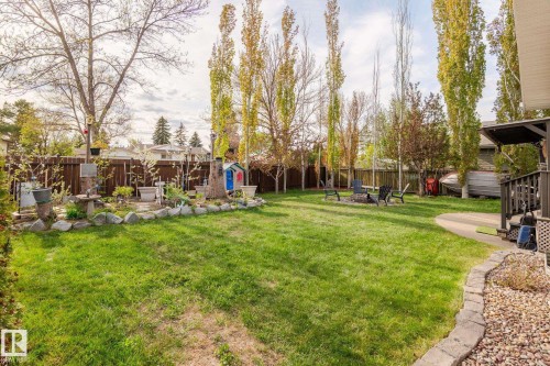 Expansive backyard featuring a lush lawn, established trees, a stone-edged garden bed, a fire pit area, and a covered deck with railing - 15232 120 Nw, Edmonton, AB 