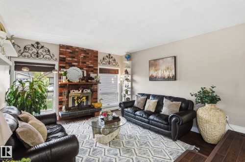 Inviting living area featuring a brick-clad fireplace, dark wood-finish flooring, and large windows with horizontal blinds - 15232 120 Nw, Edmonton, AB 