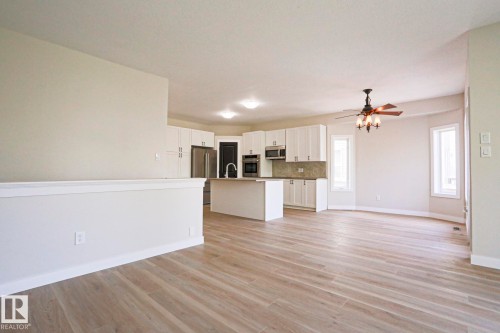 Open-concept living space featuring wood-finish flooring, a contemporary kitchen with white cabinetry and stainless steel appliances, and a central island with a sink - 82 Meadowview Point(E), Sherwood Park, AB - Indoor Photo Showing Kitchen