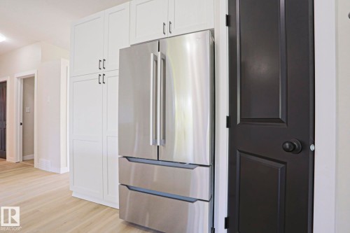 Integrated stainless steel refrigerator framed by white cabinetry with dark pulls, wood-finish flooring, and a contrasting dark paneled door - 82 Meadowview Point(E), Sherwood Park, AB - Indoor Photo Showing Kitchen