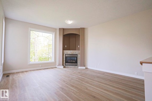 Bright living space featuring a large arched window, wood-finish flooring, and a fireplace with a tiled surround - 82 Meadowview Point(E), Sherwood Park, AB - Indoor Photo Showing Living Room With Fireplace