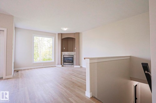 Bright living area featuring light wood-finish flooring, a corner fireplace with a tiled surround, an arched alcove, and a large picture window - 82 Meadowview Point(E), Sherwood Park, AB - Indoor With Fireplace