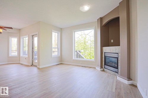 Living area featuring light wood-finish flooring, a built-in fireplace with tile surround, a large arched window with decorative grilles, multiple additional windows, and a glass-paneled door - 82 Meadowview Point(E), Sherwood Park, AB - Indoor With Fireplace