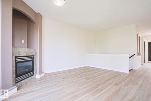 Living area featuring a corner fireplace with a tiled surround, recessed arch detail, and light wood-finish flooring - 82 Meadowview Point(E), Sherwood Park, AB - Indoor With Fireplace