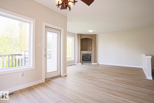 Spacious room featuring wood-finish flooring, a contemporary fireplace with an arched niche, and a ceiling fan with integrated lighting - 82 Meadowview Point(E), Sherwood Park, AB - Indoor With Fireplace