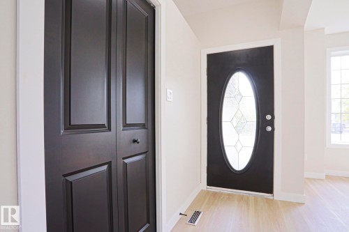 Entryway featuring a black front door with an oval leaded glass insert, light wood-finish flooring, white baseboards, and a black paneled bifold closet door - 82 Meadowview Point(E), Sherwood Park, AB - Indoor Photo Showing Other Room