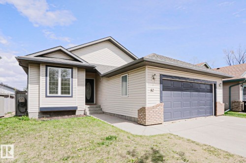 Front exterior featuring light-colored siding, a dark gray garage door, and a concrete driveway - 82 Meadowview Point(E), Sherwood Park, AB - Outdoor