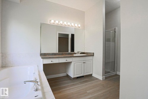 Bathroom featuring a built-in soaking tub with tile surround, a vanity with an integrated sink and countertop, a large wall-mounted mirror, and a glass-enclosed shower - 82 Meadowview Point(E), Sherwood Park, AB - Indoor Photo Showing Bathroom