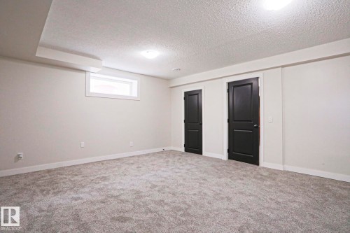 Spacious carpeted room featuring a neutral wall palette, white trim, and two dark paneled doors - 82 Meadowview Point(E), Sherwood Park, AB - Indoor