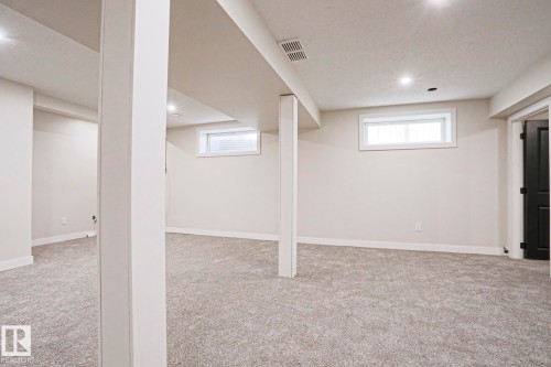Spacious lower level featuring plush gray carpeting, recessed ceiling lighting, two egress windows with white blinds, and a dark paneled door - 82 Meadowview Point(E), Sherwood Park, AB - Indoor Photo Showing Basement