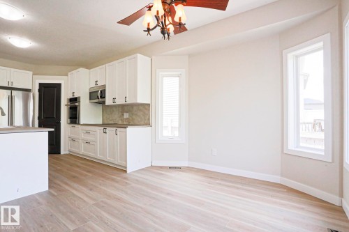 Open-concept kitchen and dining area featuring light wood-finish flooring, white cabinetry, stainless steel appliances, and a central kitchen island - 82 Meadowview Point(E), Sherwood Park, AB - Indoor Photo Showing Kitchen