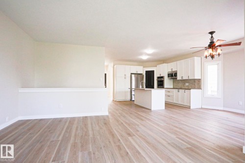 Open-concept living space featuring wood-finish flooring, a contemporary kitchen island, stainless steel appliances, white cabinetry with dark hardware, and a ceiling fan with integrated lighting - 82 Meadowview Point(E), Sherwood Park, AB - Indoor Photo Showing Kitchen