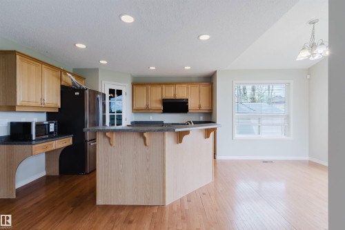 Spacious kitchen featuring wood-finish cabinetry, a central island with countertop seating, stainless steel appliances, and wood-finish flooring - 3534 Mclean Crescent, Edmonton, AB - Indoor Photo Showing Kitchen