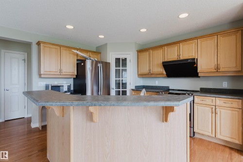 Kitchen featuring light wood cabinetry, stone-finish countertops, stainless steel appliances, and wood-finish flooring - 3534 Mclean Crescent, Edmonton, AB - Indoor Photo Showing Kitchen