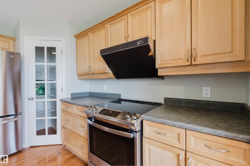 Kitchen featuring wood-finish cabinetry, dark countertops, and stainless steel appliances including a range with overhead vent - 3534 Mclean Crescent, Edmonton, AB - Indoor Photo Showing Kitchen