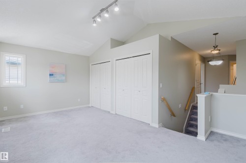 Vaulted ceiling with track lighting illuminates a carpeted room featuring two bifold door closets and a window with blinds - 3534 Mclean Crescent, Edmonton, AB - Indoor Photo Showing Other Room